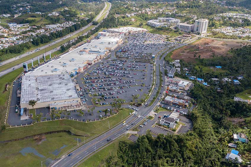 Aerial view of The Outlets at Montehiedra shopping center and its adjacent parking lot, captured from a high vantage point.